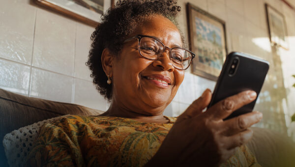 Mulher sorrindo enquanto acessa o app da Tele Sena pelo celular em casa.