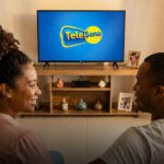 Couple sitting on a couch watching a TV that displays the Tele Sena logo.