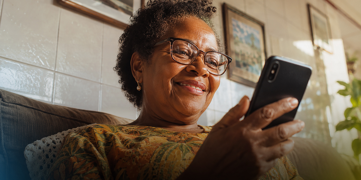 Mulher sorrindo enquanto acessa o app da Tele Sena pelo celular em casa.