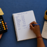 Pessoa usando calculadora e caderno para organizar as contas do mês e controlar o orçamento.