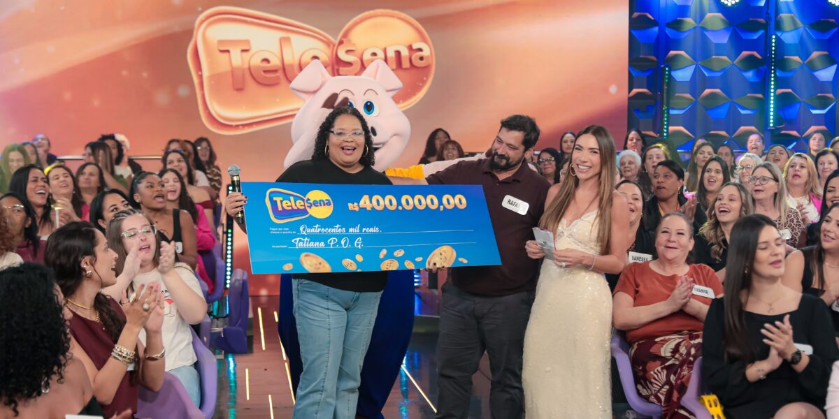 Ganhadora da Tele Sena recebe prêmio de R$ 400 mil no palco do SBT, com plateia comemorando.