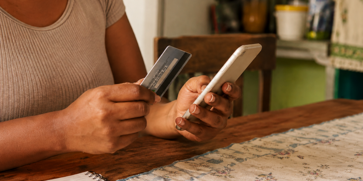 Mulher usa cartão de crédito e celular para acompanhar compras e controlar os gastos da fatura.
