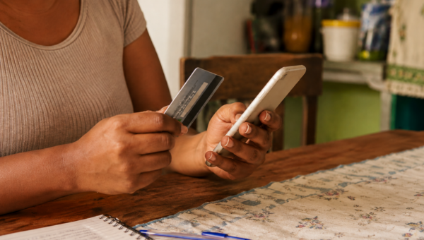 Mulher usa cartão de crédito e celular para acompanhar compras e controlar os gastos da fatura.